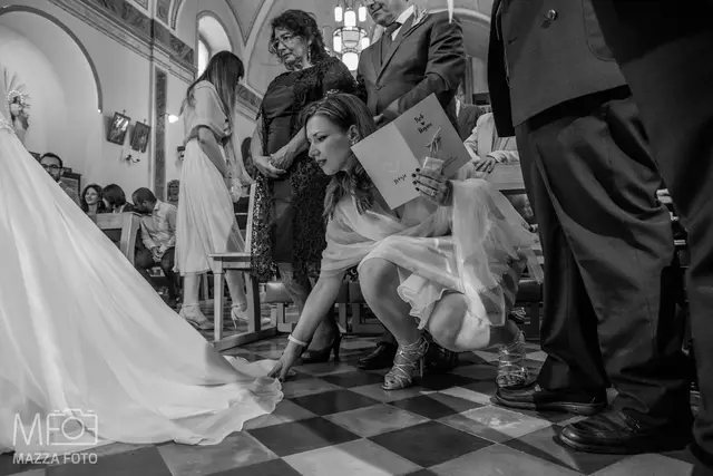 La damigella sistema l'orlo dell'abito della sposa in chiesa