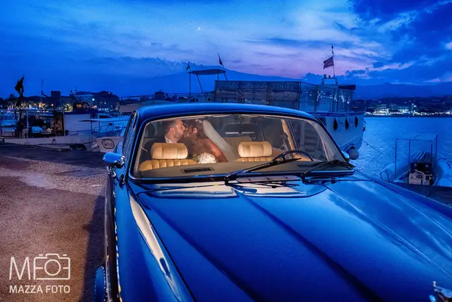 Gli sposi si baciano nell'auto d'epoca al porto, all'ora blu