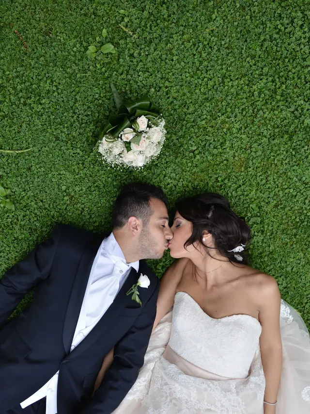 Gli sposi sdraiati sull'erba si baciano, il bouquet accanto